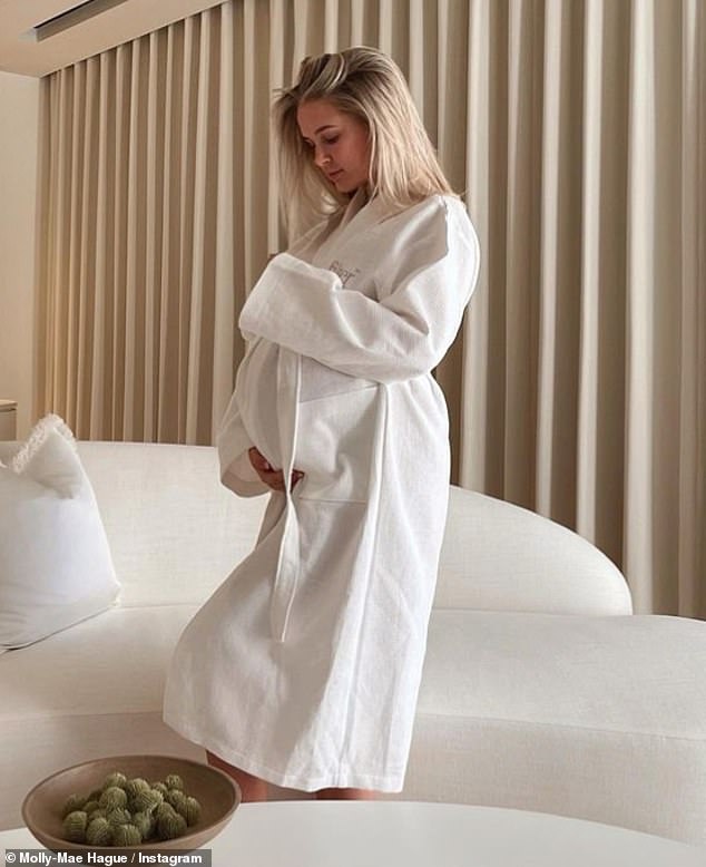 Glowing: The influencer cradled her tummy as she wrapped herself in a white robe while posing in front of a chaise longue