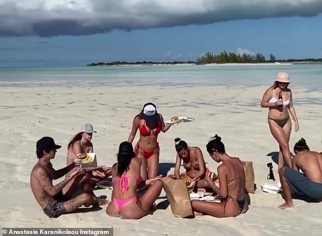 Island vibes: Surrounded by her glamorous friends, the model posted a video of herself sitting on an endless stretch of white sand, eating and drinking in the sunshine as island music played in the background