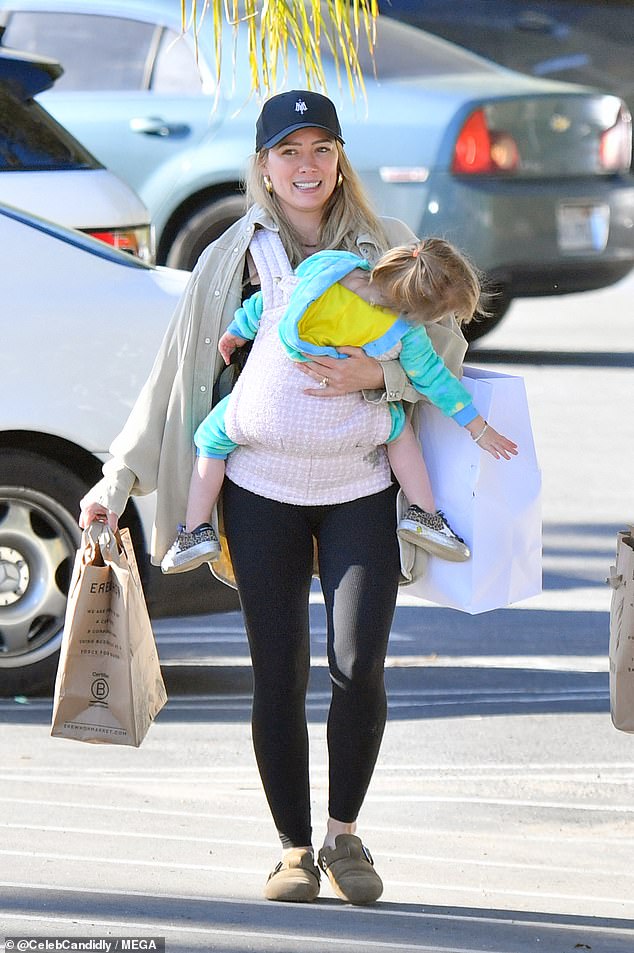 Bundle of joy: Their daughter Mae wore a blue and yellow jumpsuit with a pair of shiny black sneakers as she sat in the pink and white plaid baby carrier