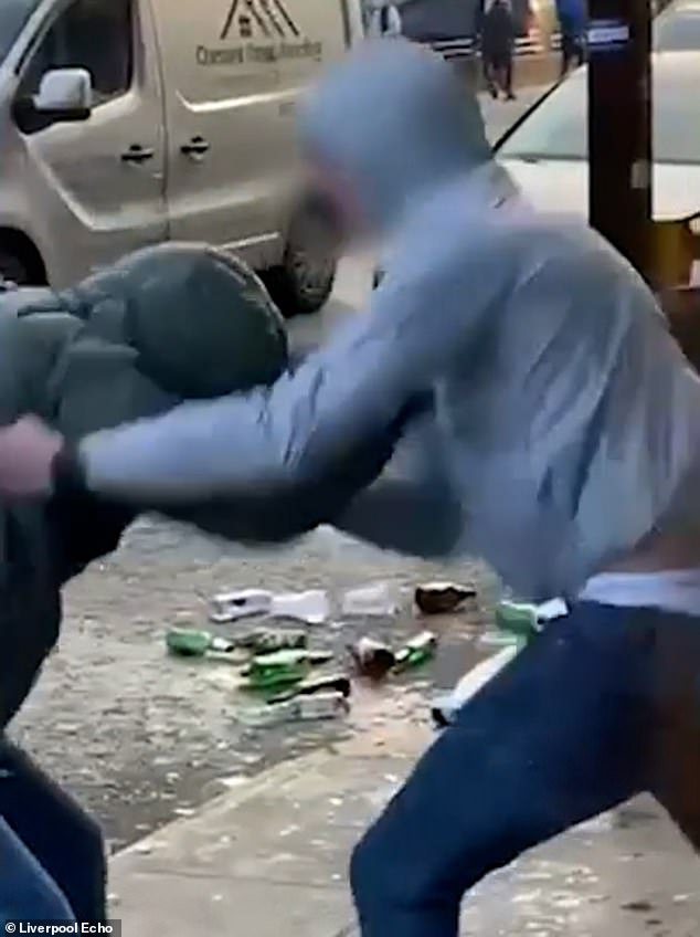 A man in a gray hoodie can be seen throwing an aggressive punch directly at another person's face.