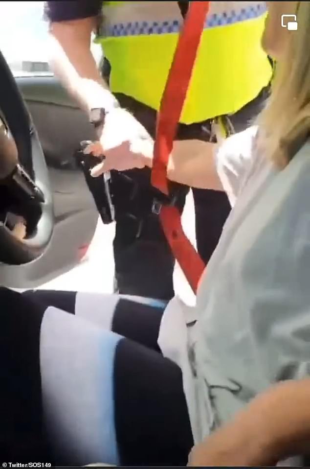 The woman passes the phone to her passenger so he can continue recording as she is taken out of the vehicle.