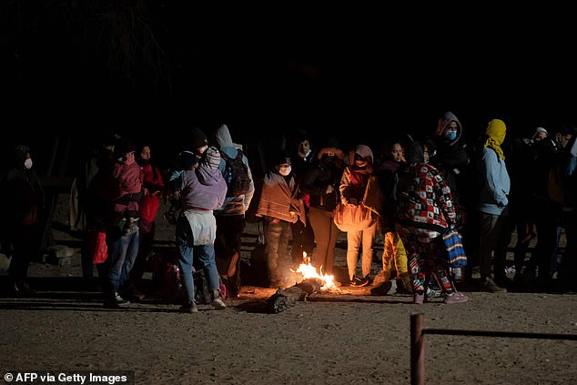 Asylum seekers try to warm up by a small campfire as they wait to be processed by a US Customs and Border Patrol agent near the US-Mexico border fence near Somerton, Arizona, on June 26. December 2022