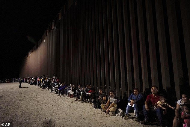 Migrants wait along a border wall after crossing from Mexico, near Yuma, Arizona, on August 23, 2022.