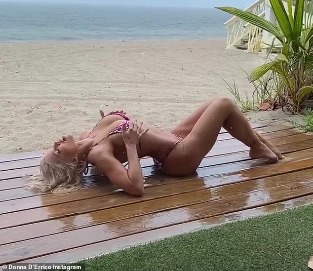 Sizzling: The 54-year-old Baywatch vet sprawled out on a wooden board by the beach as water rained down on her toned physique