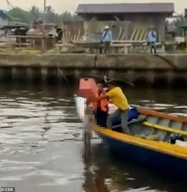 The reptile, normally one of nature's most ruthless killers, left the boy next to a boat, where two men are seen lifting the body on board.