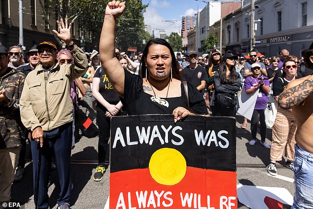 A protester carries a banner displaying the Aboriginal flag during an Invasion Day rally in Sydney.