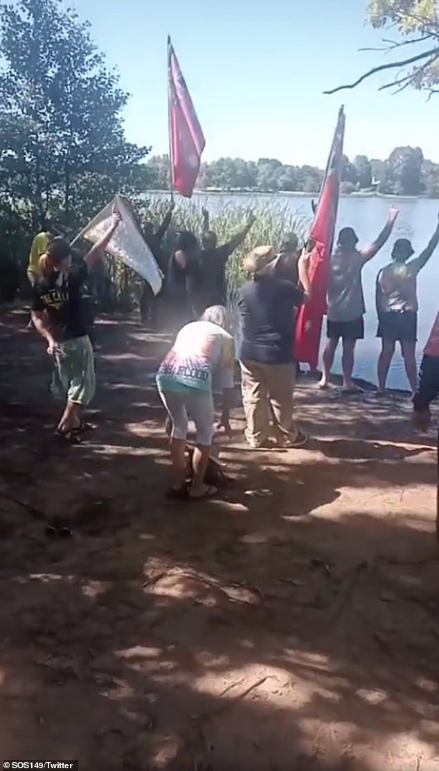 Unite for White protesters gather on the shores of Lake Burley Griffin and raise their arms, sing songs and hymns, and chant slogans about conspiracy theories.