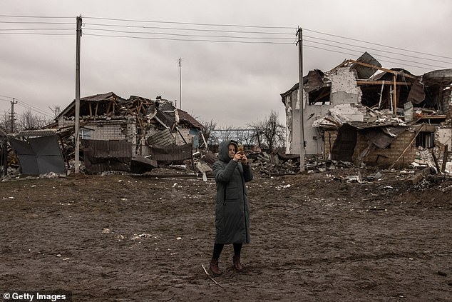 A woman takes photos with her mobile phone next to residential houses damaged after Russian missile attacks.