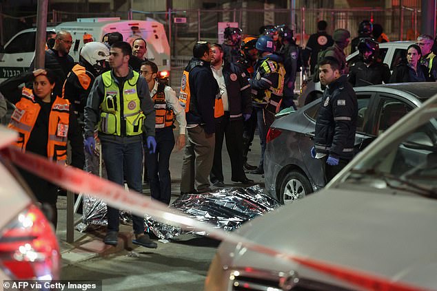 Emergency service personnel and Israeli security forces stand near a covered body at the site of a reported attack in an Israeli-annexed East Jerusalem settler neighborhood, on January 27, 2023.