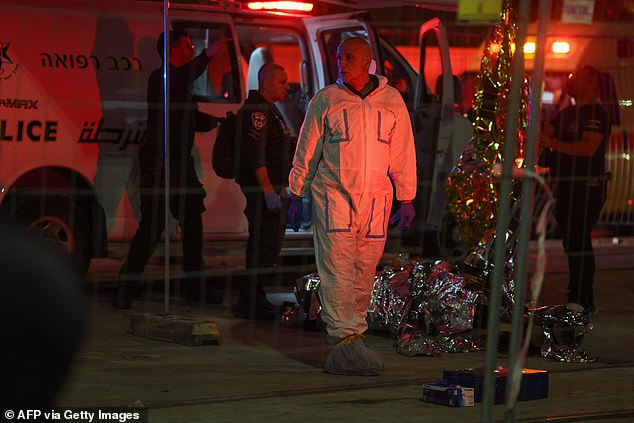 Israeli emergency service personnel and security forces stand near a covered body at the site of a reported attack in an Israeli-annexed East Jerusalem settler neighborhood, January 27, 2023.