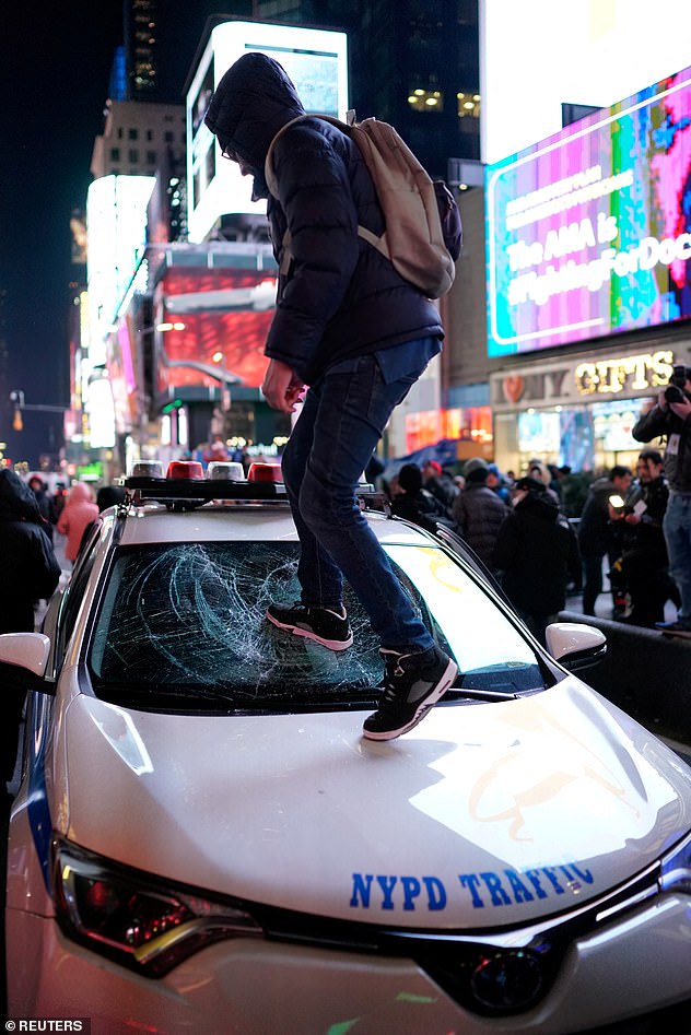 A protester was seen standing on a clearly vandalized front window of a police car in New York City.