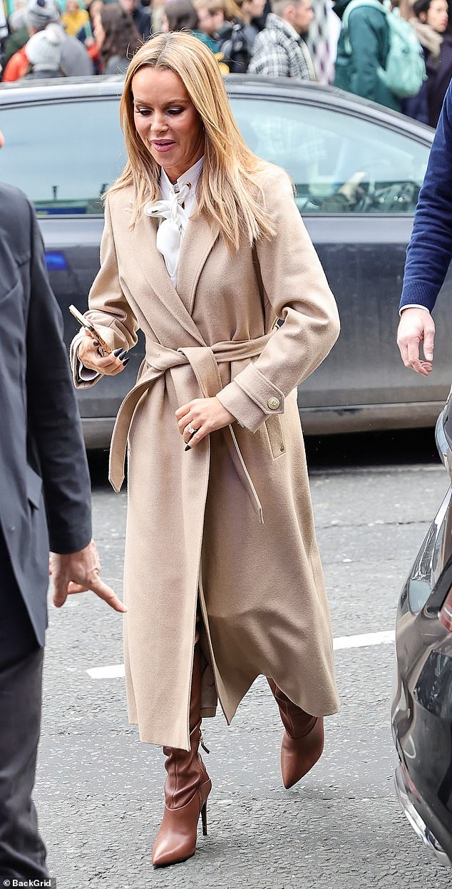 Chic: Amanda looked effortlessly chic in a white bowtie top and beige jacket, while giving herself a few extra inches in brown knee-high boots