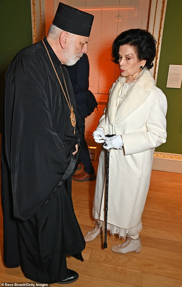 Elegant: She looked elegant in a long white coat paired with a detailed white dress and gold earrings (pictured meeting right Rev. Kenneth Nowakowski)