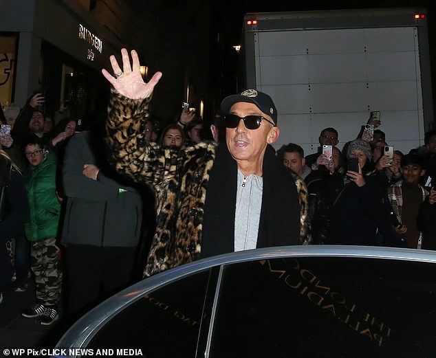 Smile and wave: She kept it cozy in a pair of black boots and finished her look with a navy baseball cap and square sunglasses.