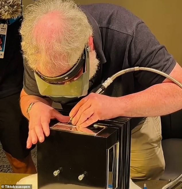 As the Serbian ace claims victory, a busy engraver can be seen working on the Norman Brooks Challenge Cup and inscribing Djokovic's name and country of origin.