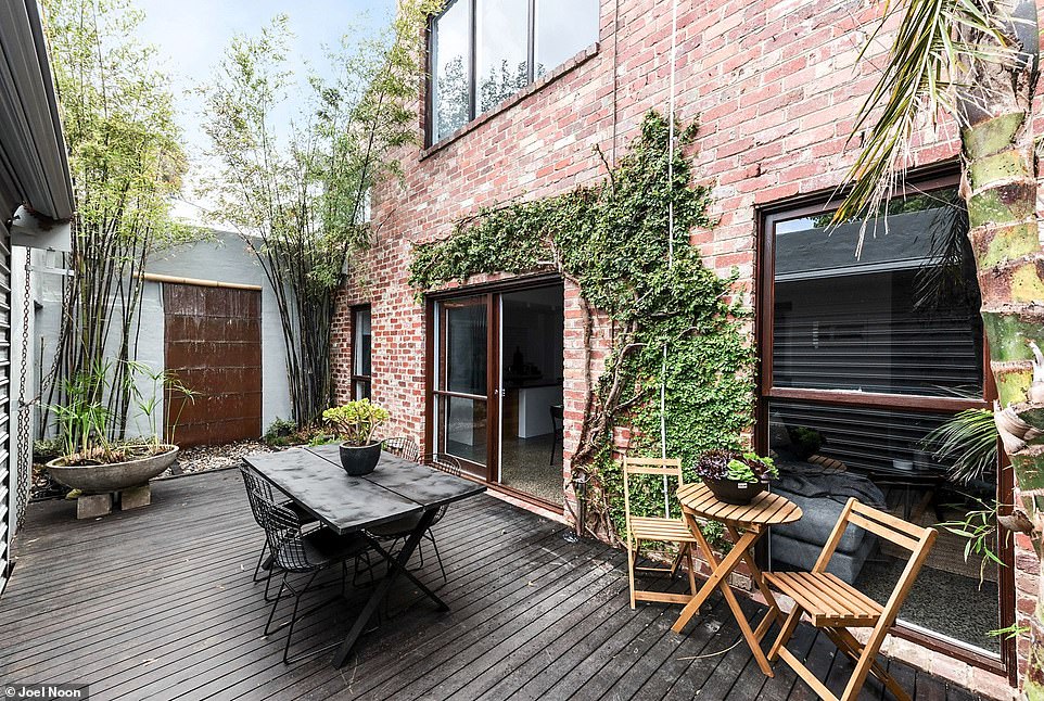 Leafy vines climb the brick wall on the outdoor entertaining platform that has a trickling water fountain and towering bamboo trees