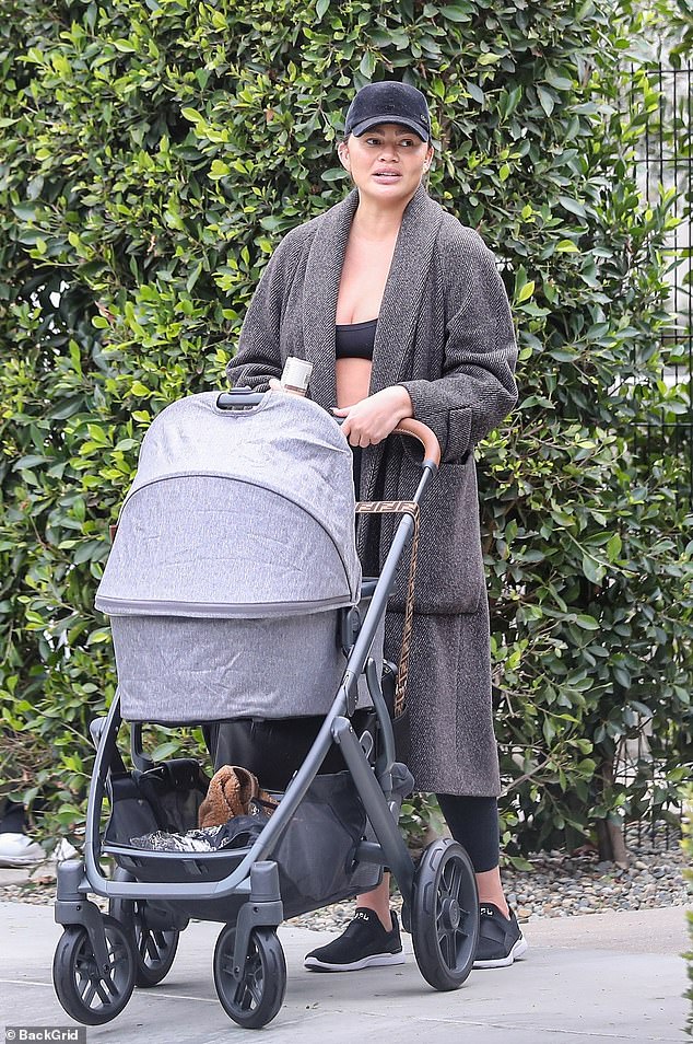 Braving the rain: Her youngest son clung to her side as Teigen held her hand while the oldest carried a rainbow-polka dotted clear umbrella over her head