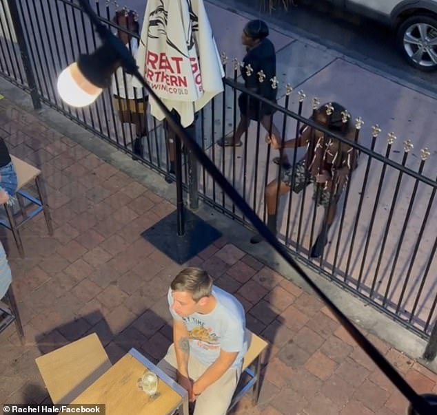 The moment the girl on the left in the white T-shirt spits through the fence at a young man drinking in the pub's beer garden