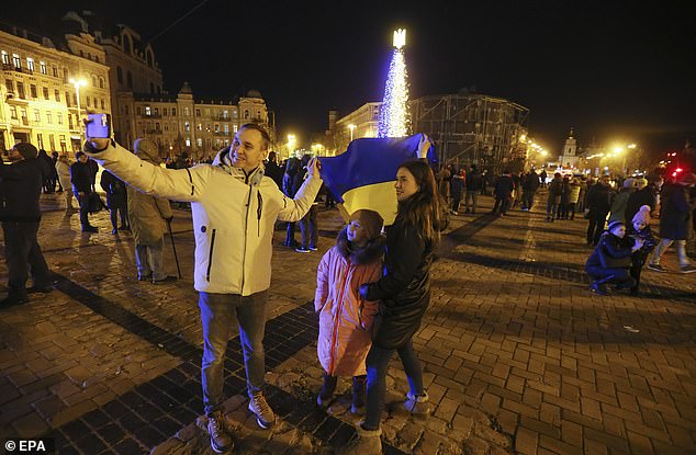 Ukrainians take a selfie with the Ukrainian national flag near a Christmas tree at night in central Kyiv, Ukraine on December 31, 2022 before the New Year