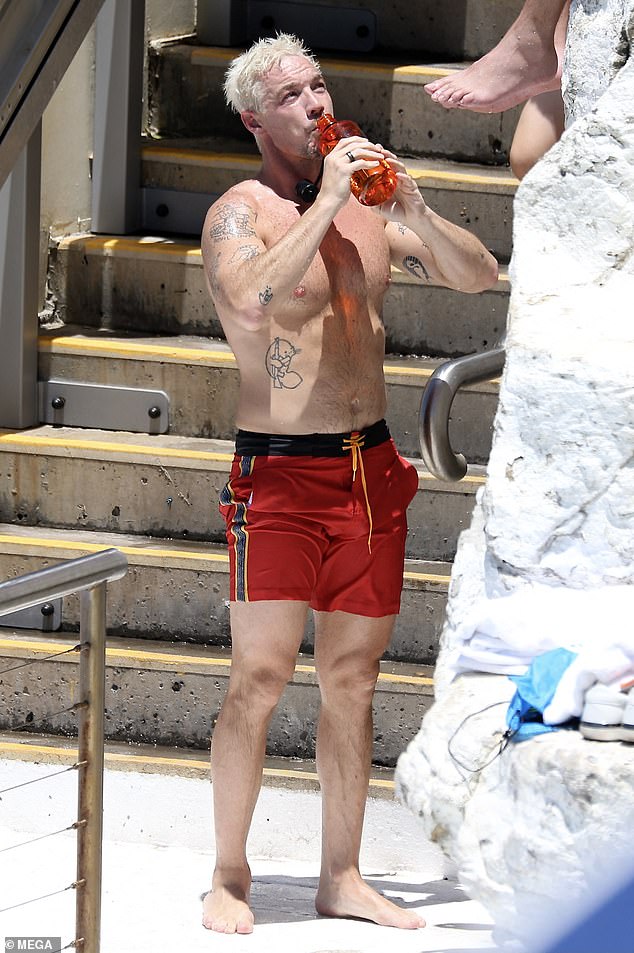 Shirtless DJ Diplo, 44, (pictured) showed off his muscular chest and extensive collection of tattoos while enjoying a swim in a pair of skintight red shorts at Icebergs Pool in Sydney on Monday.