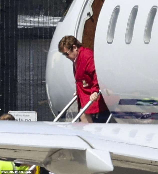 Elton John, 75, donned a bright red jacket while flying to Sydney with his sons Zachary and Elijah after celebrating New Year's Eve in Queensland.