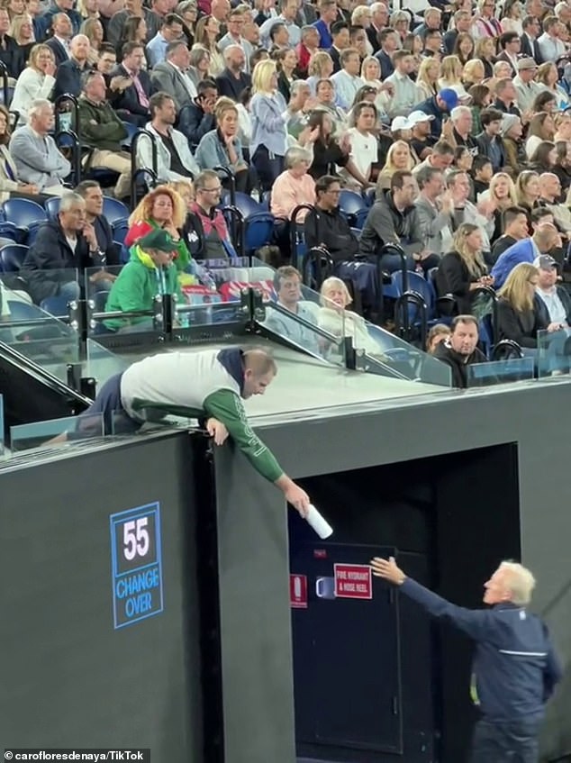 A member of Djokovic's team hands the bottle with the newly affixed label to a tournament official for delivery during play in the second round of the Australian Open.