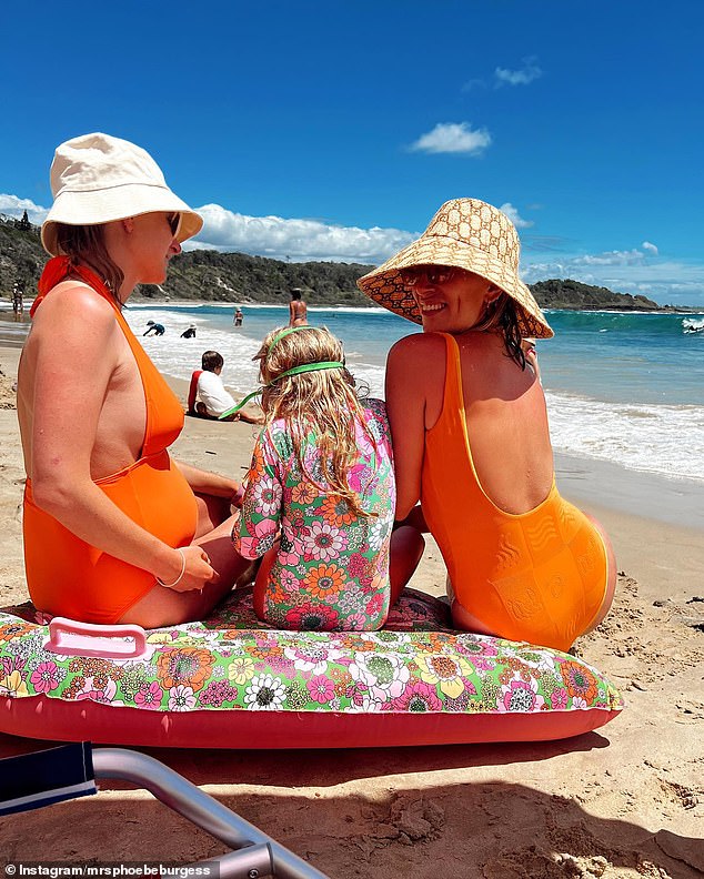 Phoebe Burgess is enjoying her summer with her two children and her family.  The former WAG turned influencer showed off her figure in a bright orange swimsuit during a beach getaway on Friday.  She is pictured with her daughter Poppy and her sister Harriet.