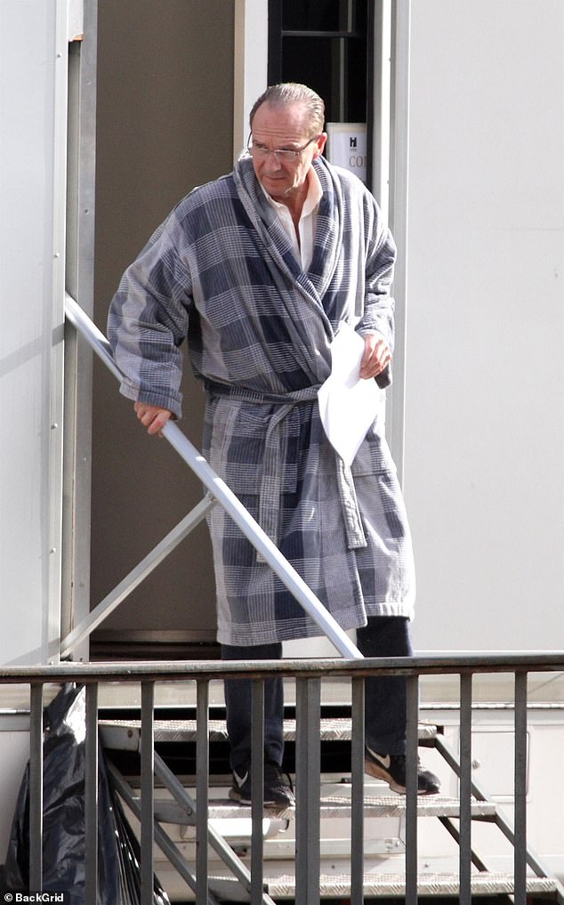 On location: Ralph Fiennes stepped out of his trailer in a robe while taking a break between filming scenes for his new movie Conclave in Rome on Thursday.