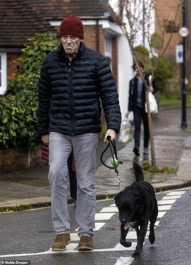 Hugh Laurie, pictured wearing a red hat, was seen walking around with a slightly embarrassed expression.