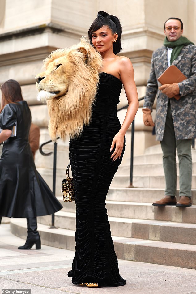 Kylie Jenner sported a massive lion's head attached to her black dress when she made a quirky appearance at the star-studded Schiaparelli show during Paris Fashion Week.  The 25-year-old reality star turned heads with the oversized stuffed animal accessory as she posed up a storm while heading to the venue on Monday.  The faux animal was sewn onto the front of a sleek, figure-hugging black velvet gown with an elegant strapless design.