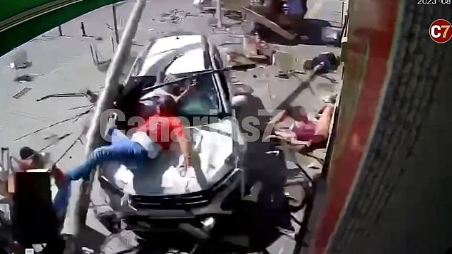 A man in a red T-shirt and blue jeans (center) landed on the hood of the vehicle as the car pulled onto the cafe terrace