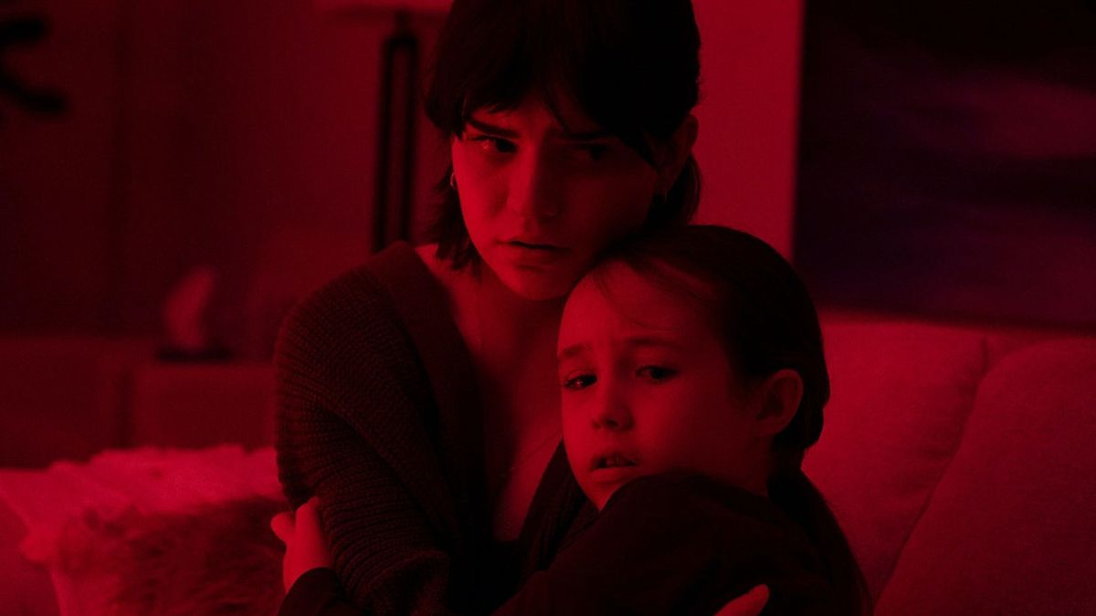 (L-R) Sophie Thatcher and Vivien Lyra Blair huddle close together on a couch in the dark, bathed in a deep red light in The Boogeyman.