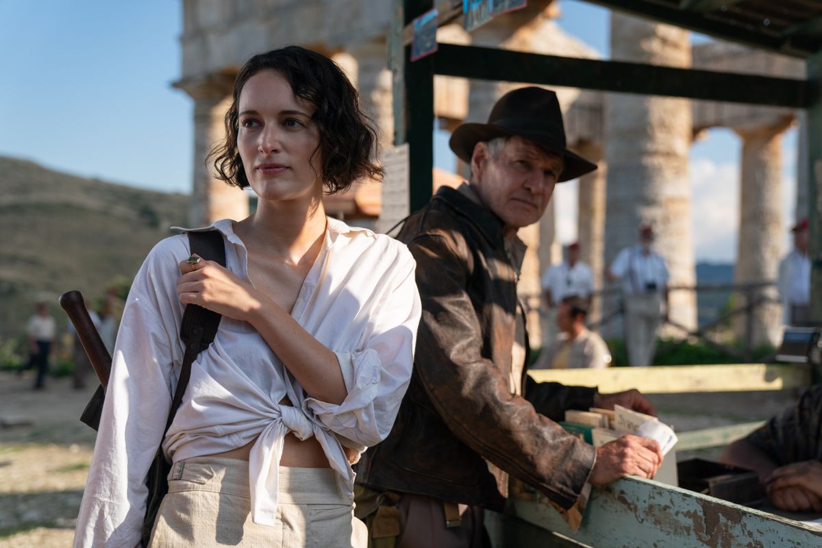 Helena Shaw (Phoebe Waller-Bridge, in a white button-down shirt tied to the navel) faces some ruins with Indiana Jones (Harrison Ford, dressed in his classic Indiana Jones outfit) in Indiana Jones and the Dial of Destiny.