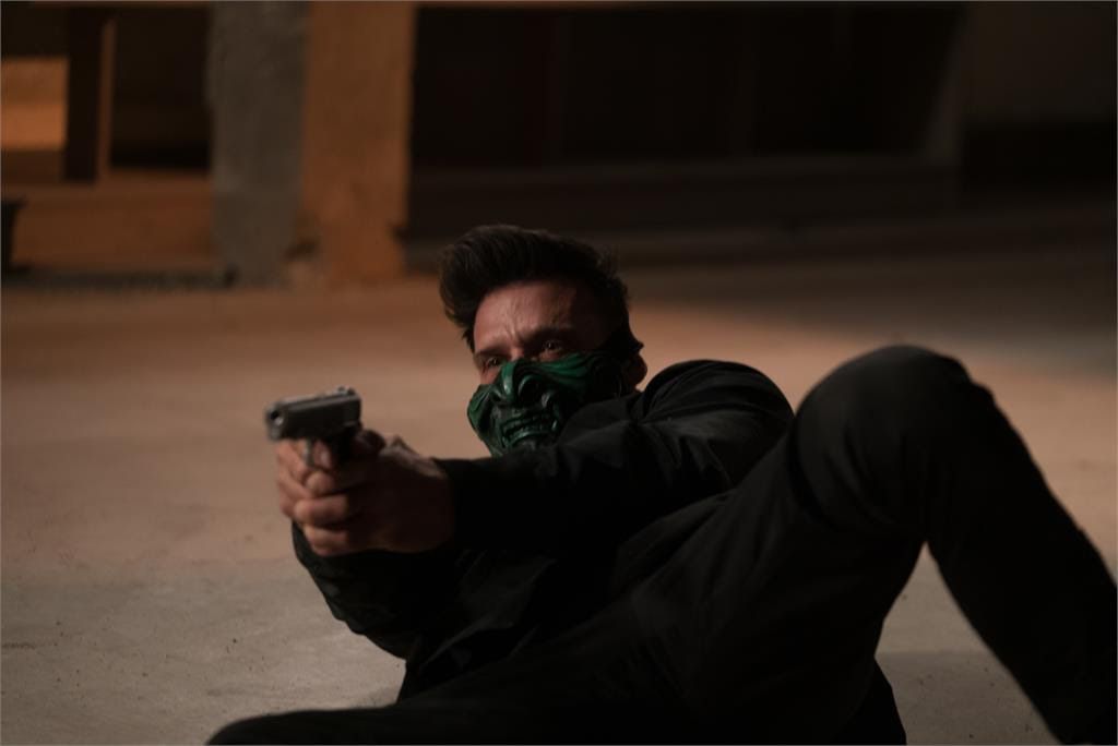 Frank Grillo, who wears a devilish green mask over the lower half of his face, aims a gun while lying on the floor in King of Killers.