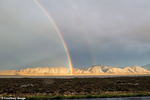 A bright and colorful rainbow stands out against the gray sky in the Nevada desert