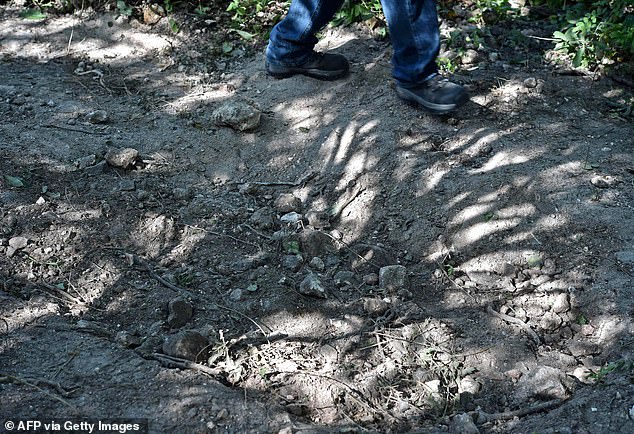 A journalist walks past a mass grave excavated by forensic personnel to recover bodies at an alleged drug camp used to bury victims of the massacre