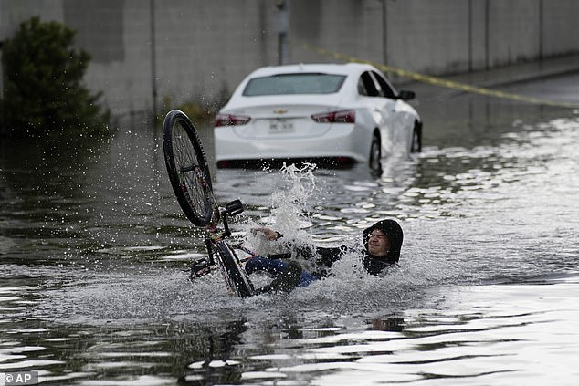 A cyclist falls Friday while trying to ride through the water near a stranded car in Las Vegas