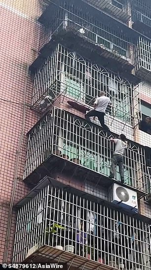 In phone footage of the daring rescue, the child tries to free herself with her hands as brave neighbors climb up the front of the building to reach her.