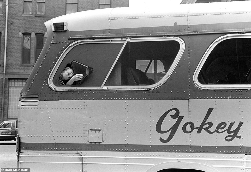 A young girl smiles as she looks out the window of a bus