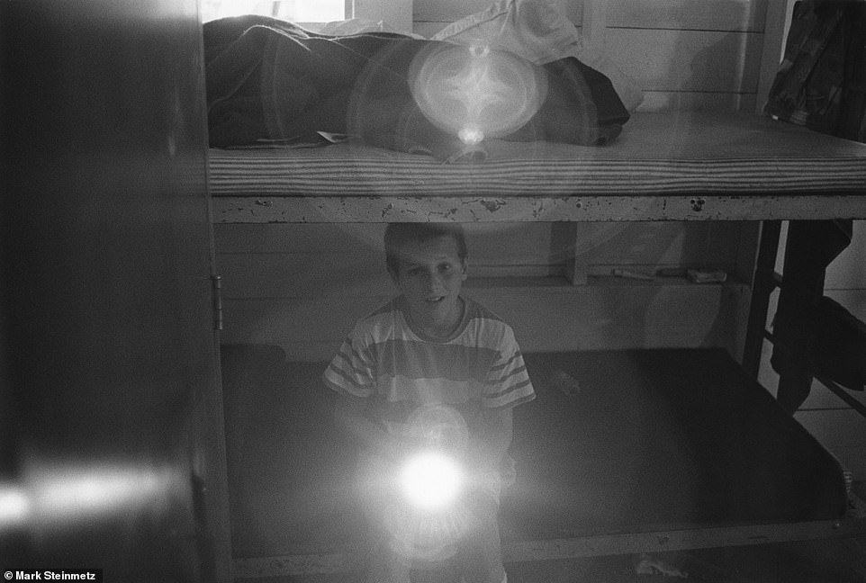 A young boy sitting on the edge of a bed shines a flashlight into Steinmetz's camera