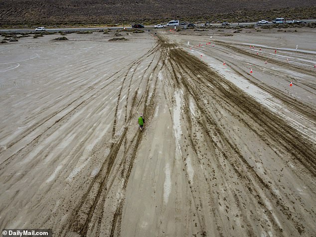 Thousands of Burning Man visitors trudged through sloppy mud on Saturday — many barefoot or with plastic bags on their feet — as flooding storms swept through the Nevada desert