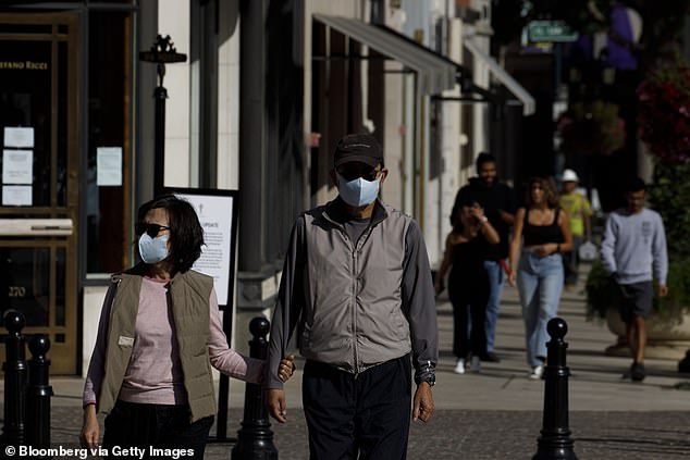 People wear protective masks as they walk in front of luxury stores on Rodeo Drive in Beverly Hills on May 19, 2020