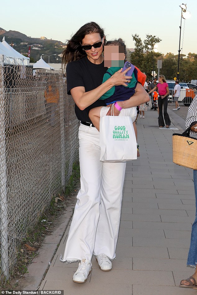 Carnival chic: Kloss tucked her statuesque six-foot post-baby body into a simple black T-shirt, tucked into white wide-leg jeans and matching $100 Adidas 