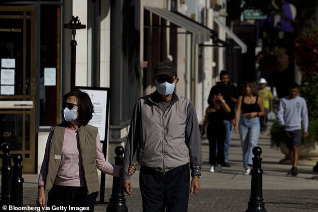 People wear protective masks as they walk in front of luxury stores on Rodeo Drive in Beverly Hills on May 19, 2020