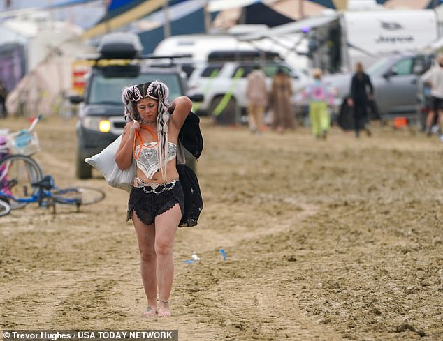 California's Martha Diaz walks along a muddy road at Burning Man carrying platform shoe bags