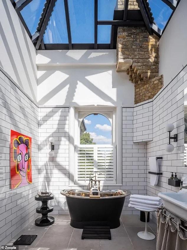 The colorful artwork continues in this large bathroom, which also features a roll-top bath and partially exposed brickwork