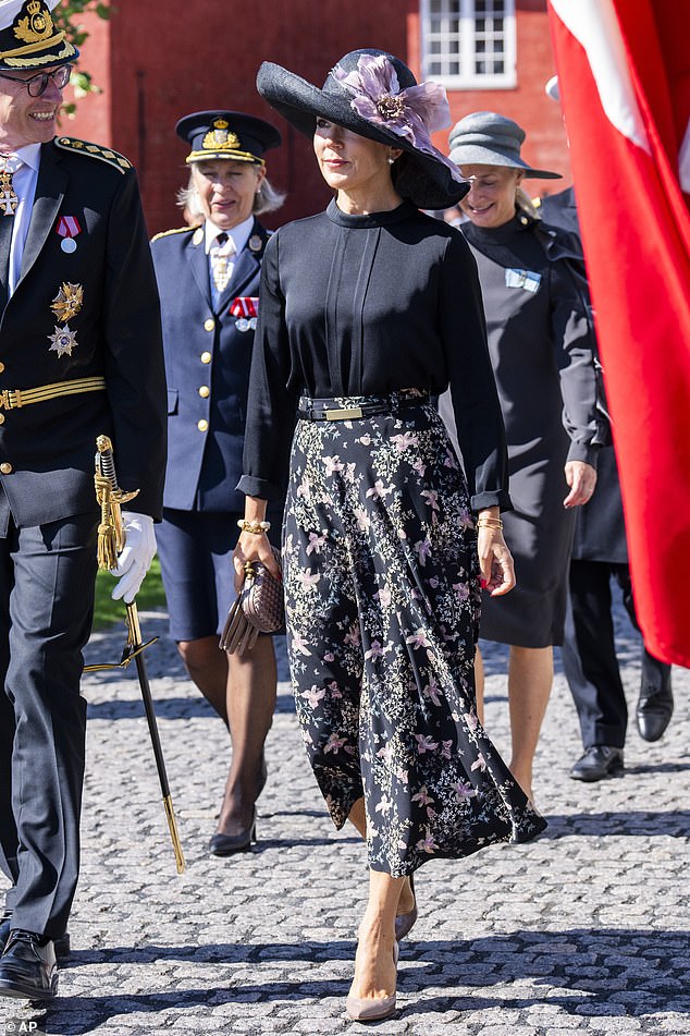 She paired the elegant ensemble with a wide-brimmed navy blue hat and a striking purple flower