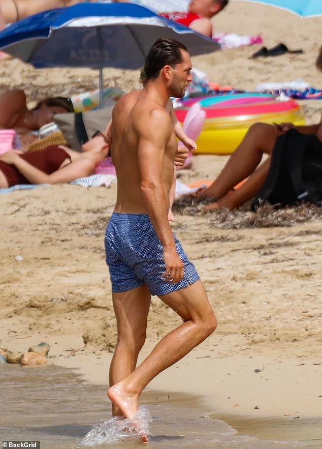 Toned: Lewis showed off his muscular body in full while wearing blue patterned board shorts