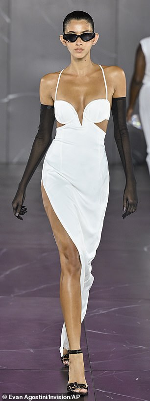 A model walks the catwalk in a stylish white dress with black transparent gloves