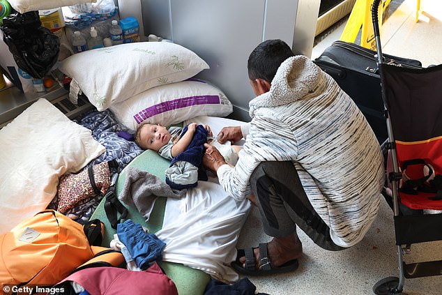 A migrant father from Venezuela changes his 15-month-old son's diaper in the lobby of a police station